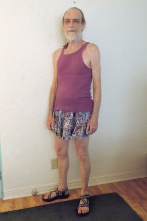 Michael Lowe Wright is wearing a short purple print skirt, purple tank top, and strappy sandals