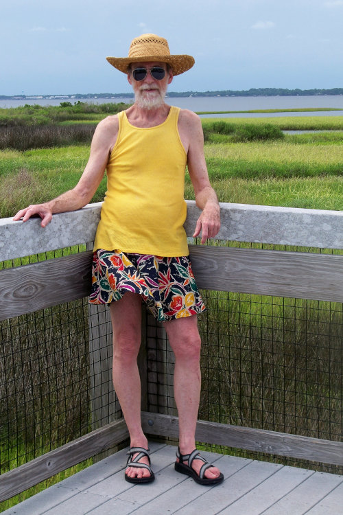 Michael Lowe Wright in a short skirt, yellow tank top, and strappy sandals at the coast