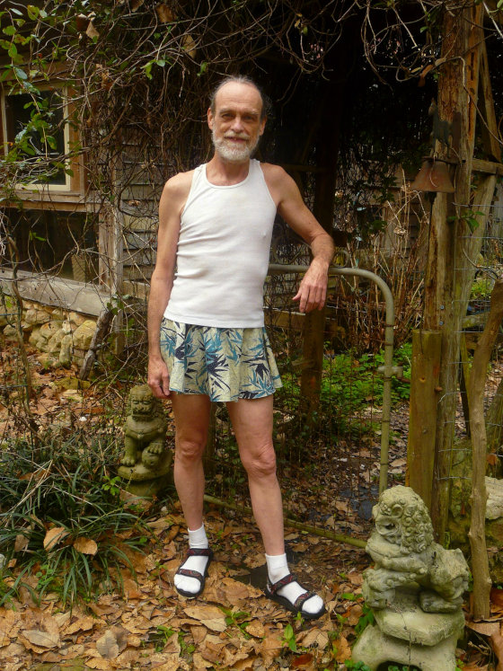 Michael Lowe Wright is wearing a tank top and short men's skirt with socks and sandals